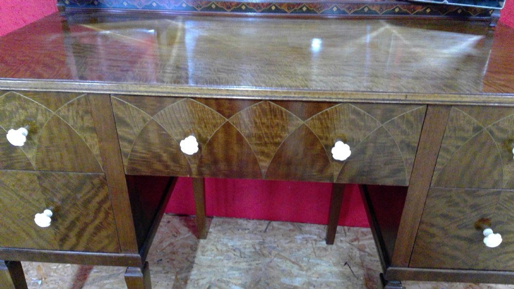 An Art Deco mahogany dressing table featuring a central mirror flanked by two adjustable wing mirrors, geometric wood inlays, and small white drawer knobs. View VI