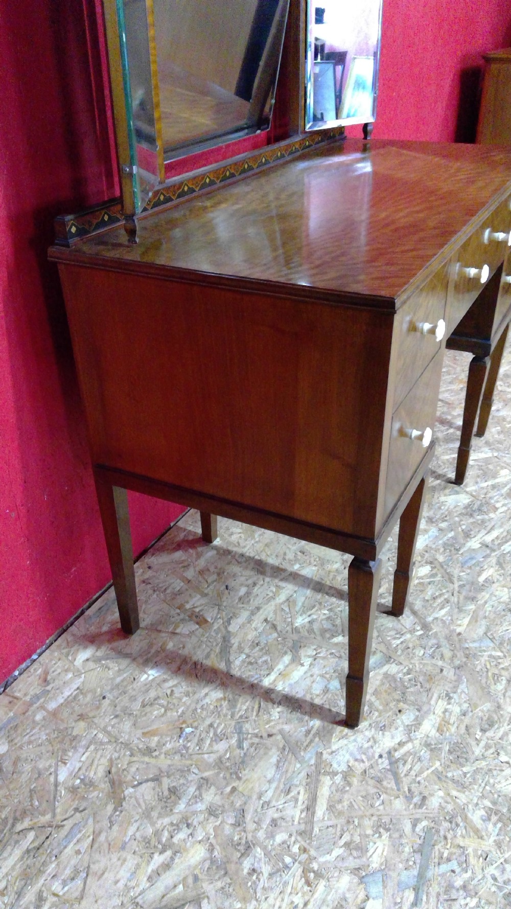An Art Deco mahogany dressing table featuring a central mirror flanked by two adjustable wing mirrors, geometric wood inlays, and small white drawer knobs. View X