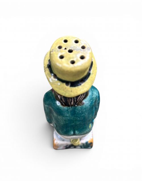 fig 1. An antique ceramic Prattware figural pepper pot depicting a male character in a yellow top hat, green coat, and pink trousers on a square base.