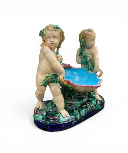 fig 1. A Victorian Minton majolica centrepiece featuring two cherub figures supporting a shell-shaped bowl with a bright turquoise interior on a green foliate base.