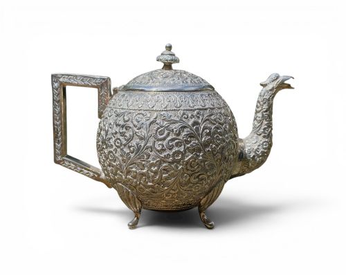 fig 1. A three-piece antique Indian silver tea service featuring detailed chased floral scrollwork, elephant-shaped lid finials, and angular geometric handles.