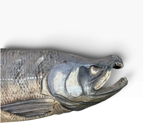 fig 1. A realistic hand-carved wooden sculpture of a salmon with detailed scales and an open mouth, finished in muted grey and brown tones.