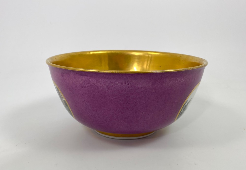 A deep porcelain bowl with a vibrant puce exterior featuring a shaped gilded frame around a hand-painted scene of two figures outdoors. View III