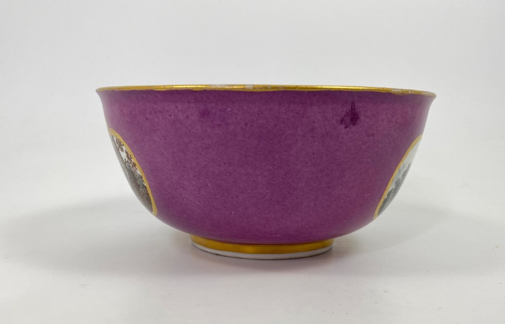 A deep porcelain bowl with a vibrant puce exterior featuring a shaped gilded frame around a hand-painted scene of two figures outdoors. View V