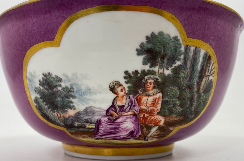 A deep porcelain bowl with a vibrant puce exterior featuring a shaped gilded frame around a hand-painted scene of two figures outdoors. View X