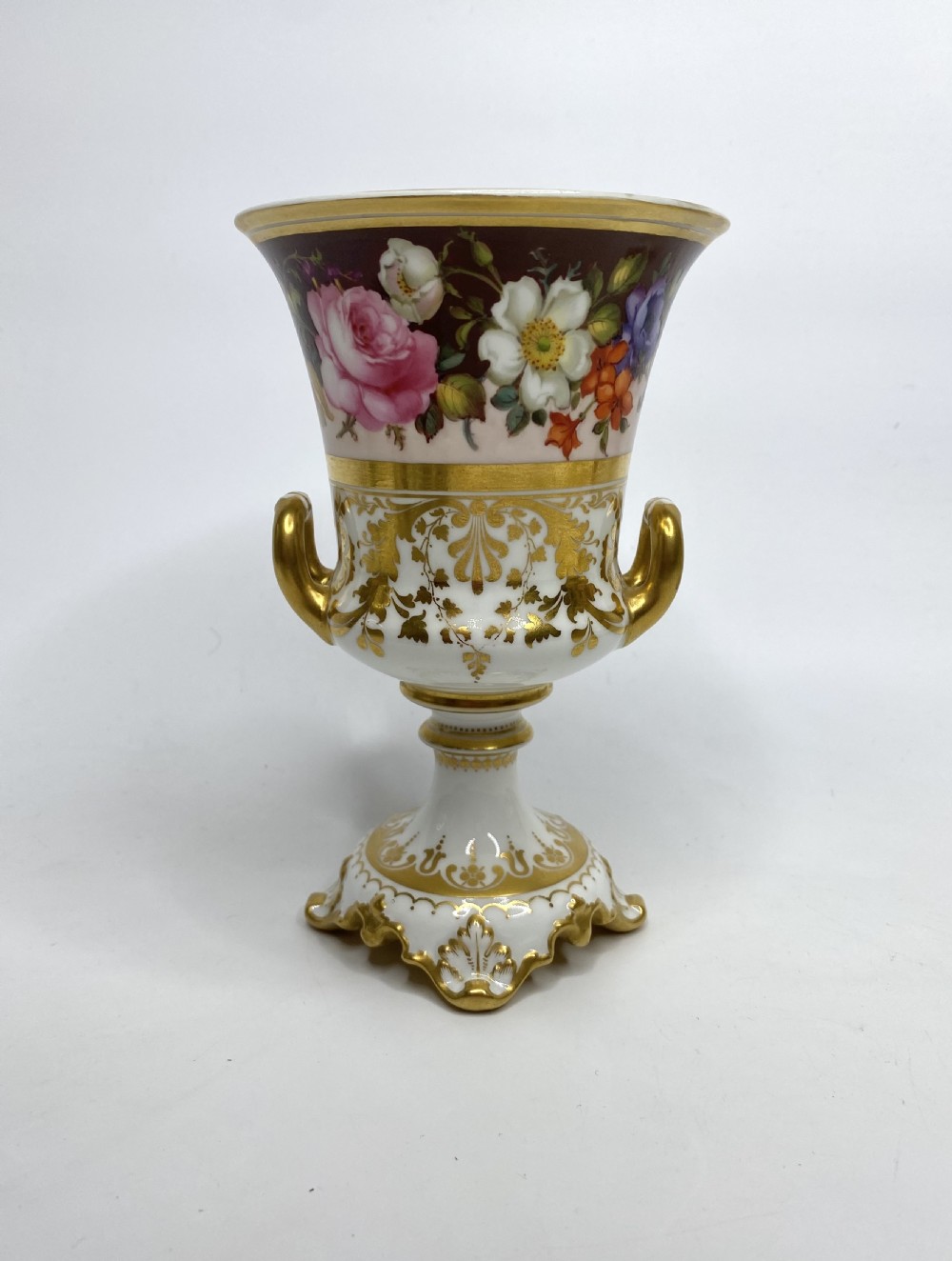 A pair of Royal Crown Derby porcelain urns featuring elaborate gold scrollwork and detailed hand-painted floral bands. View II