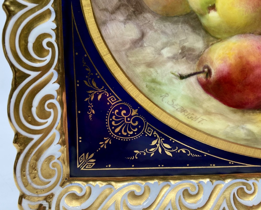 A square Royal Worcester porcelain tray featuring a central oval hand-painted fruit study framed by a dark cobalt blue ground with gold tooling and a pierced gilt scrollwork border. View V
