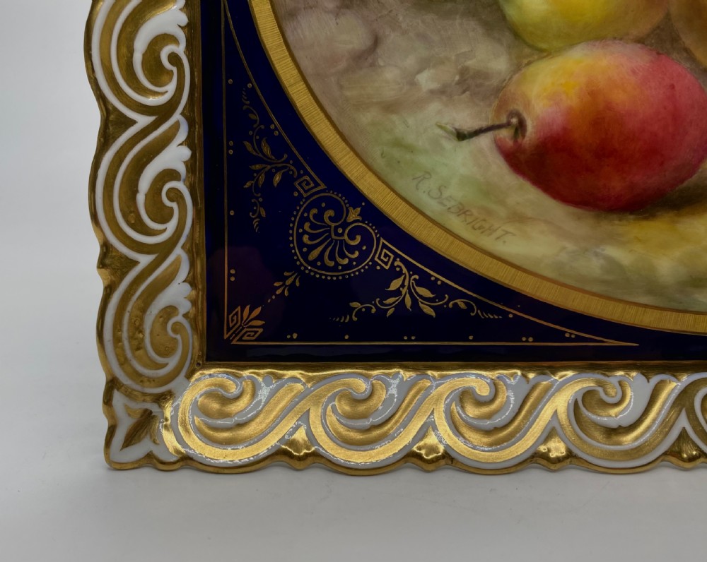 A square Royal Worcester porcelain tray featuring a central oval hand-painted fruit study framed by a dark cobalt blue ground with gold tooling and a pierced gilt scrollwork border. View VI