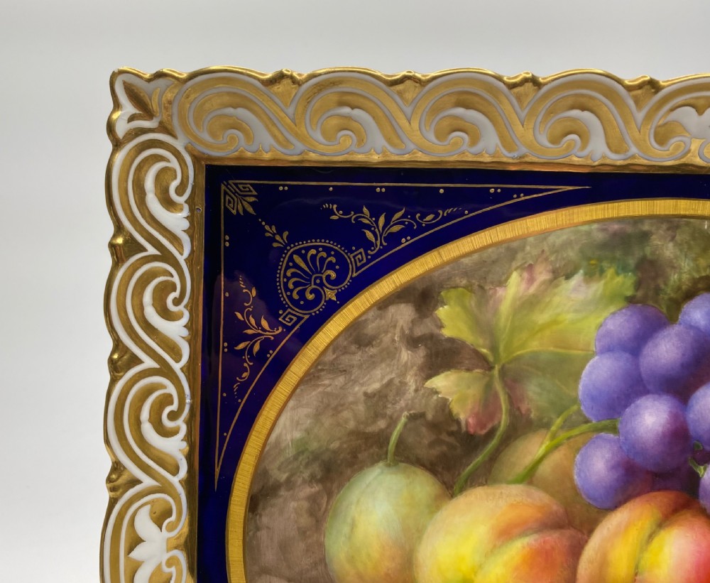 A square Royal Worcester porcelain tray featuring a central oval hand-painted fruit study framed by a dark cobalt blue ground with gold tooling and a pierced gilt scrollwork border. View VII