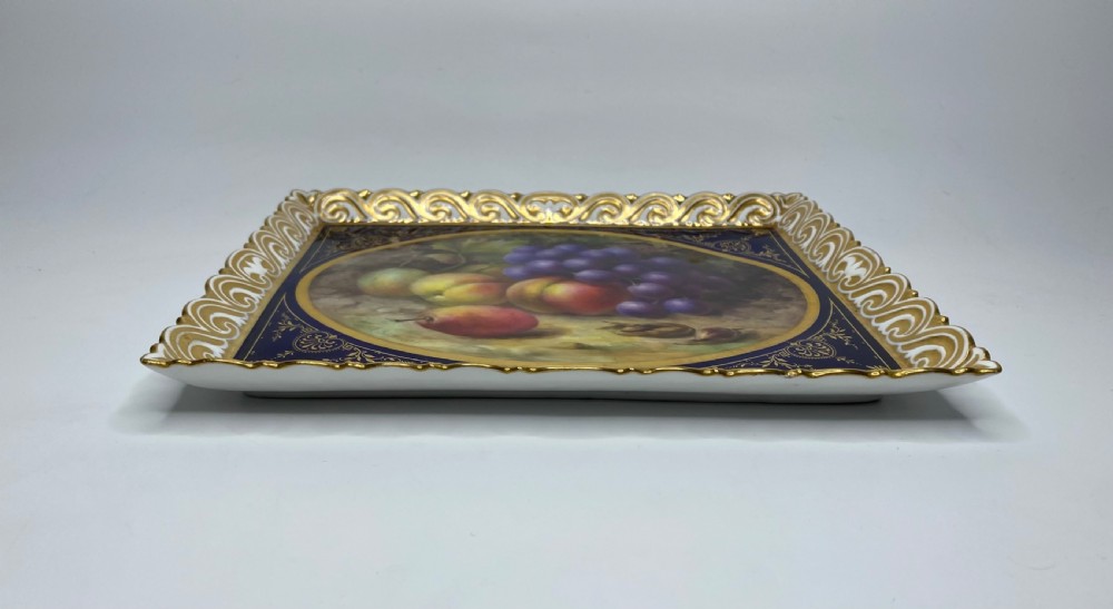A square Royal Worcester porcelain tray featuring a central oval hand-painted fruit study framed by a dark cobalt blue ground with gold tooling and a pierced gilt scrollwork border. View IX
