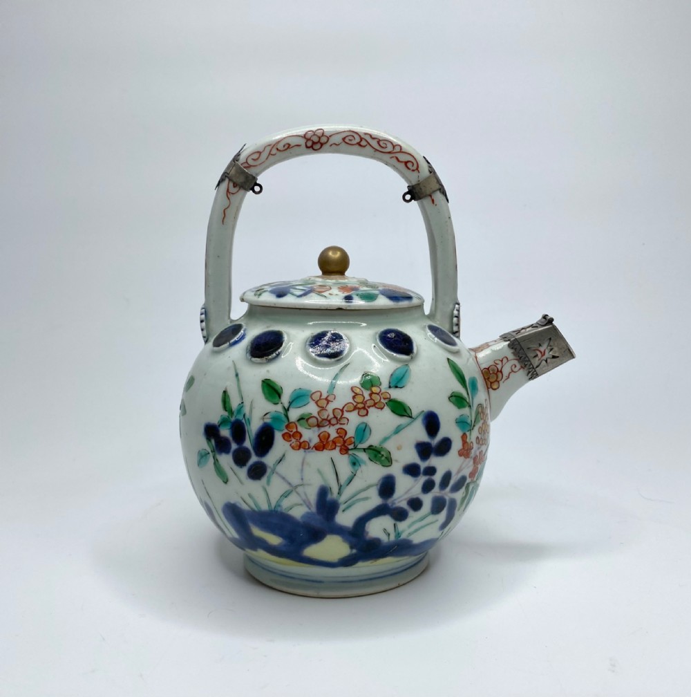An Edo-period Japanese Imari porcelain sake ewer featuring polychrome floral enamel patterns, an overhead handle, and metal mounts.