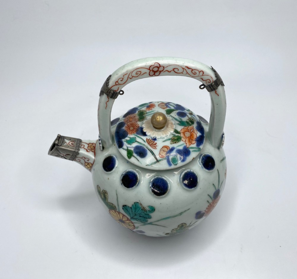 An Edo-period Japanese Imari porcelain sake ewer featuring polychrome floral enamel patterns, an overhead handle, and metal mounts. View VI