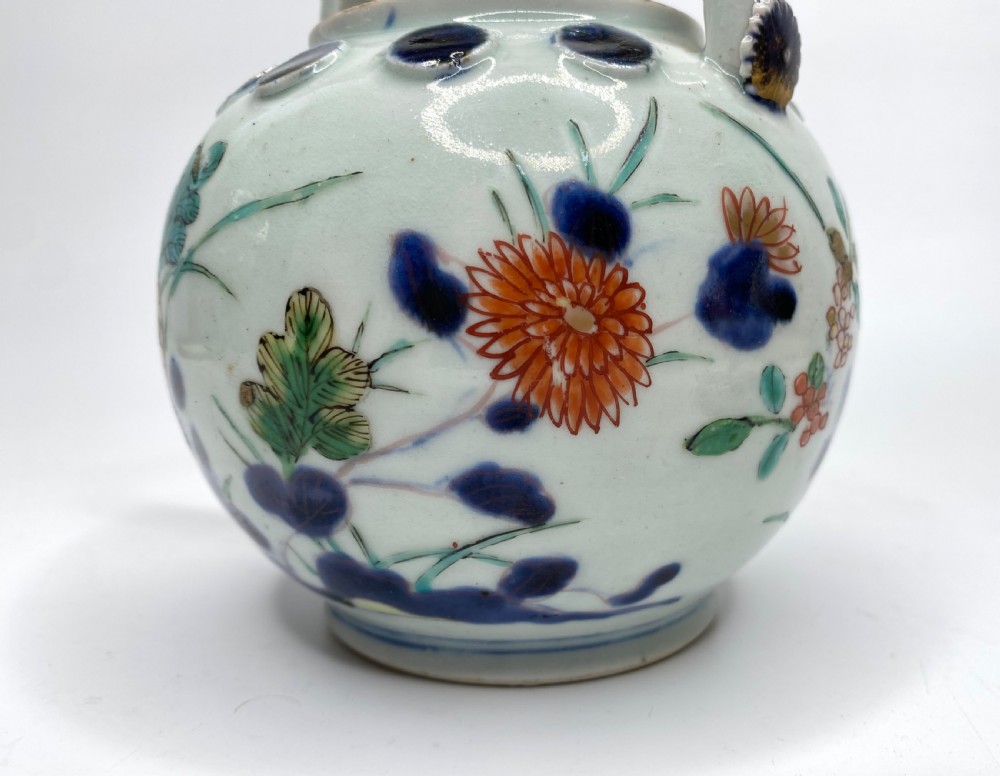 An Edo-period Japanese Imari porcelain sake ewer featuring polychrome floral enamel patterns, an overhead handle, and metal mounts. View X