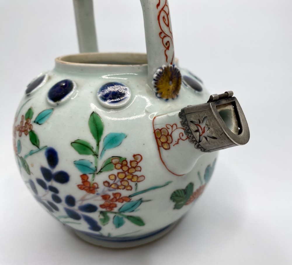 An Edo-period Japanese Imari porcelain sake ewer featuring polychrome floral enamel patterns, an overhead handle, and metal mounts. View XII