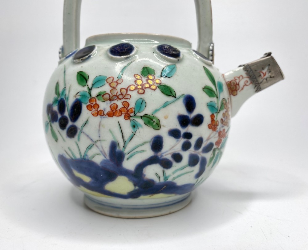 An Edo-period Japanese Imari porcelain sake ewer featuring polychrome floral enamel patterns, an overhead handle, and metal mounts. View XIII