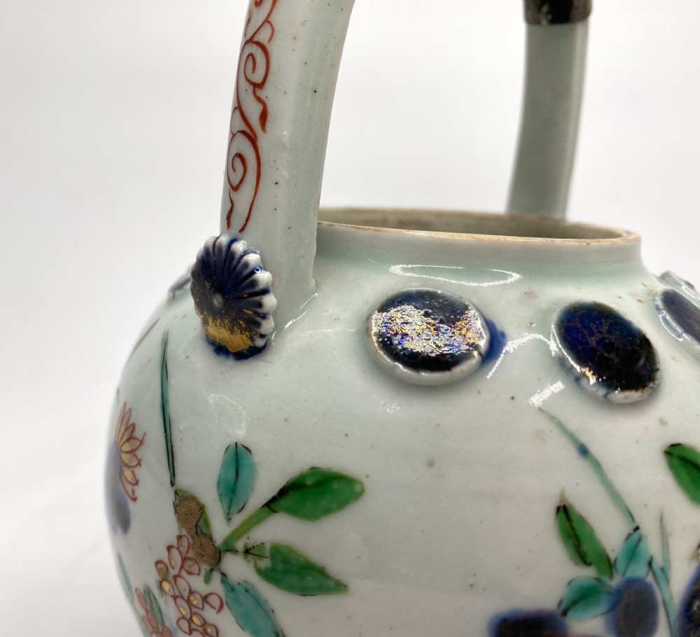 An Edo-period Japanese Imari porcelain sake ewer featuring polychrome floral enamel patterns, an overhead handle, and metal mounts. View XIV