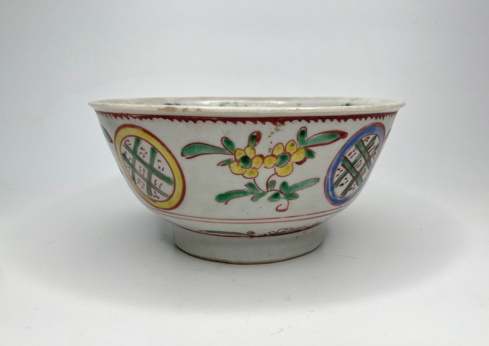 A Chinese Swatow porcelain bowl decorated with red, green, and yellow floral motifs and roundels on an off-white background.