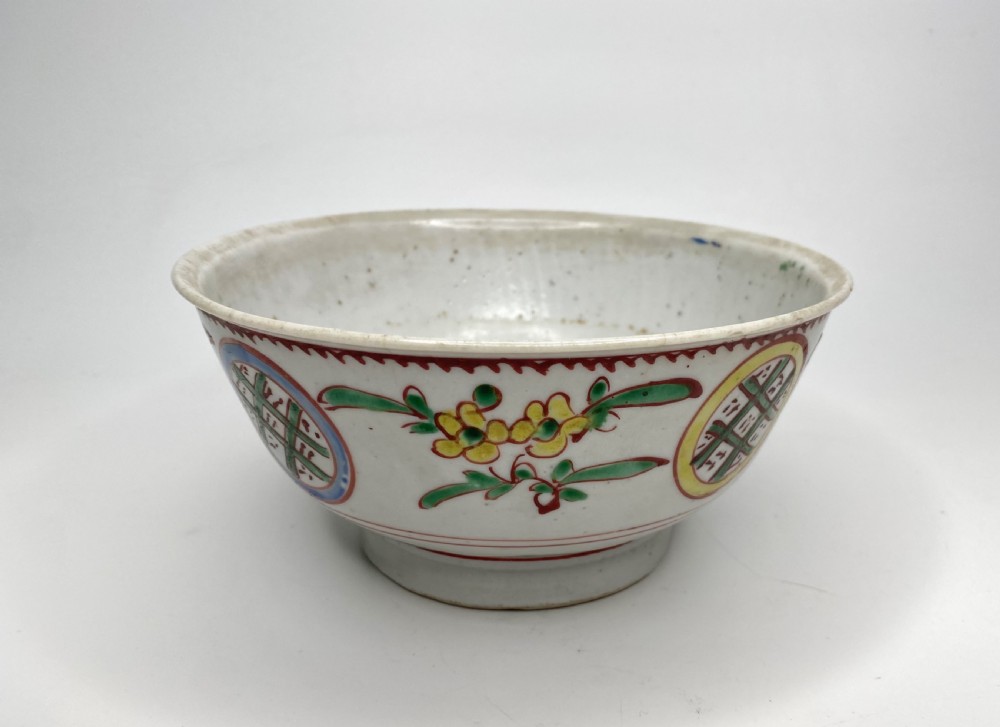 A Chinese Swatow porcelain bowl decorated with red, green, and yellow floral motifs and roundels on an off-white background. View IV