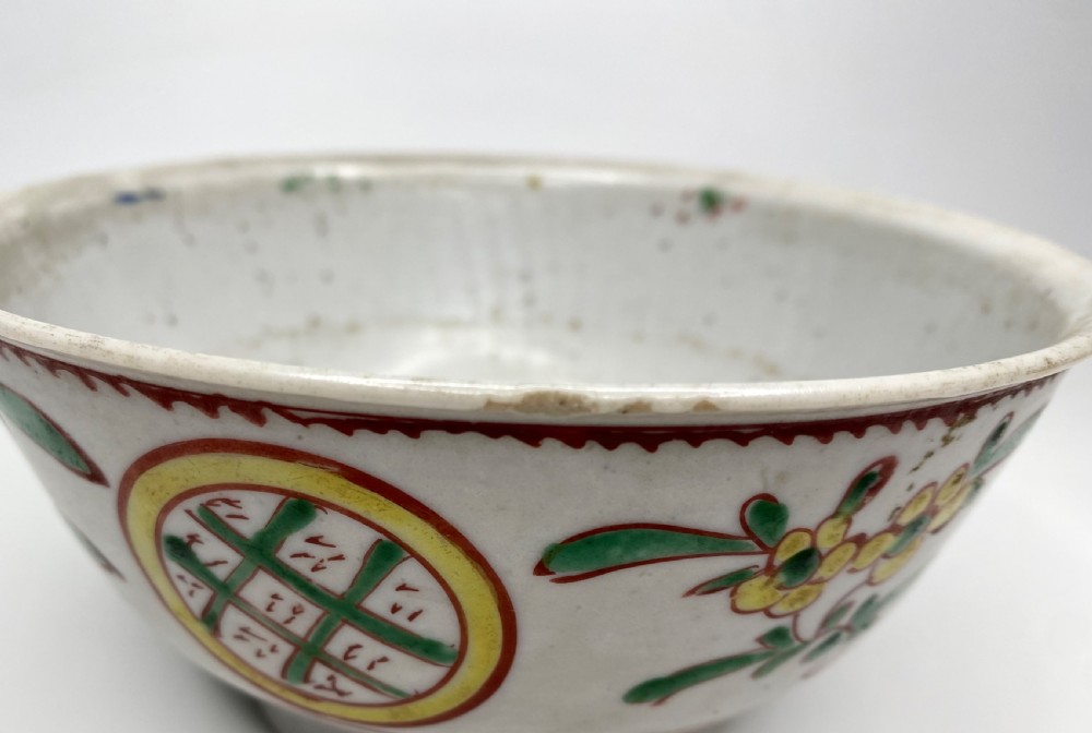 A Chinese Swatow porcelain bowl decorated with red, green, and yellow floral motifs and roundels on an off-white background. View IX