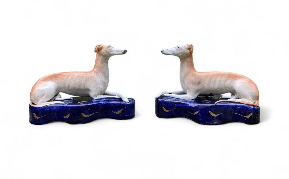 A pair of Victorian Staffordshire earthenware figures depicting recumbent tan greyhounds resting on cobalt blue bases with gilding.
