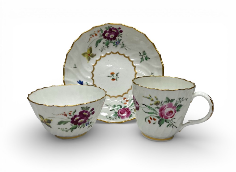 An 18th-century Worcester porcelain tea trio comprising a teacup, tea bowl, and saucer with hand-painted floral sprays and gilded spiralled moulding.