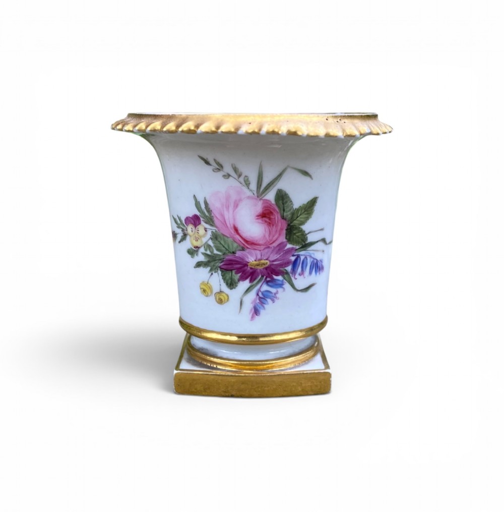 A flared white antique porcelain vase decorated with hand-painted pink and purple flowers and a square gilded pedestal base.
