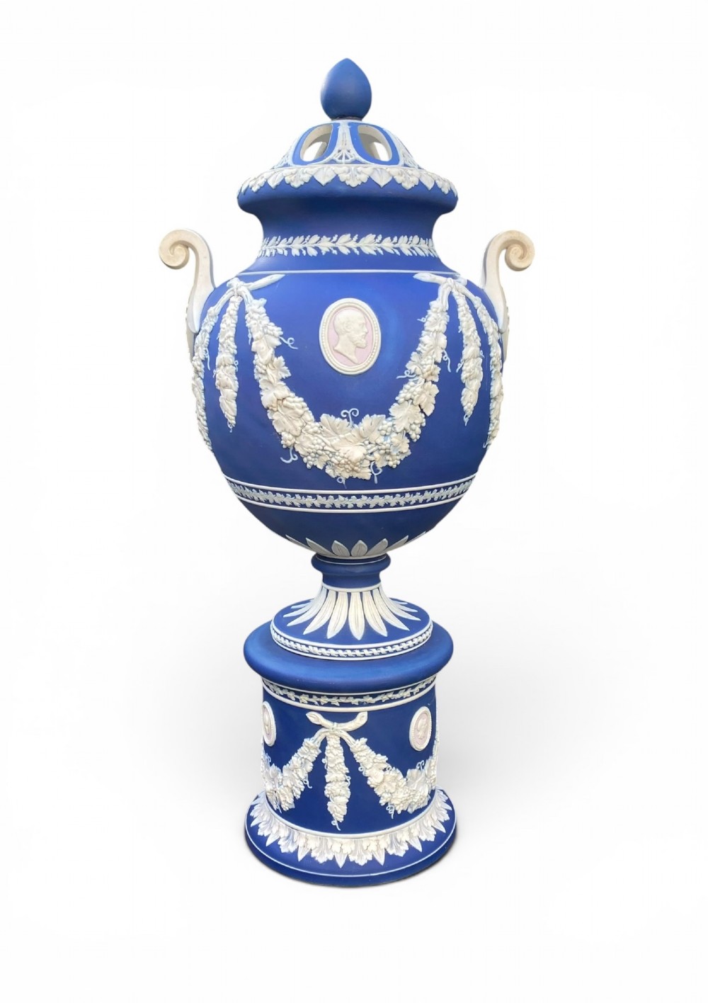 A cobalt blue jasperware pot pourri urn on a matching cylindrical pedestal, featuring white raised relief swags, classical medallions, scroll handles, and a pierced lid.