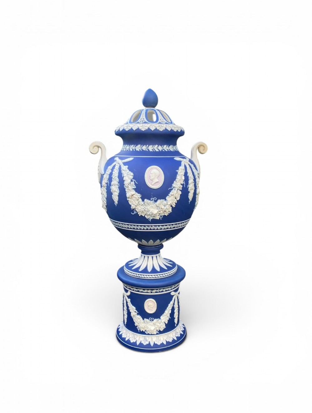 A cobalt blue jasperware pot pourri urn on a matching cylindrical pedestal, featuring white raised relief swags, classical medallions, scroll handles, and a pierced lid. View IV
