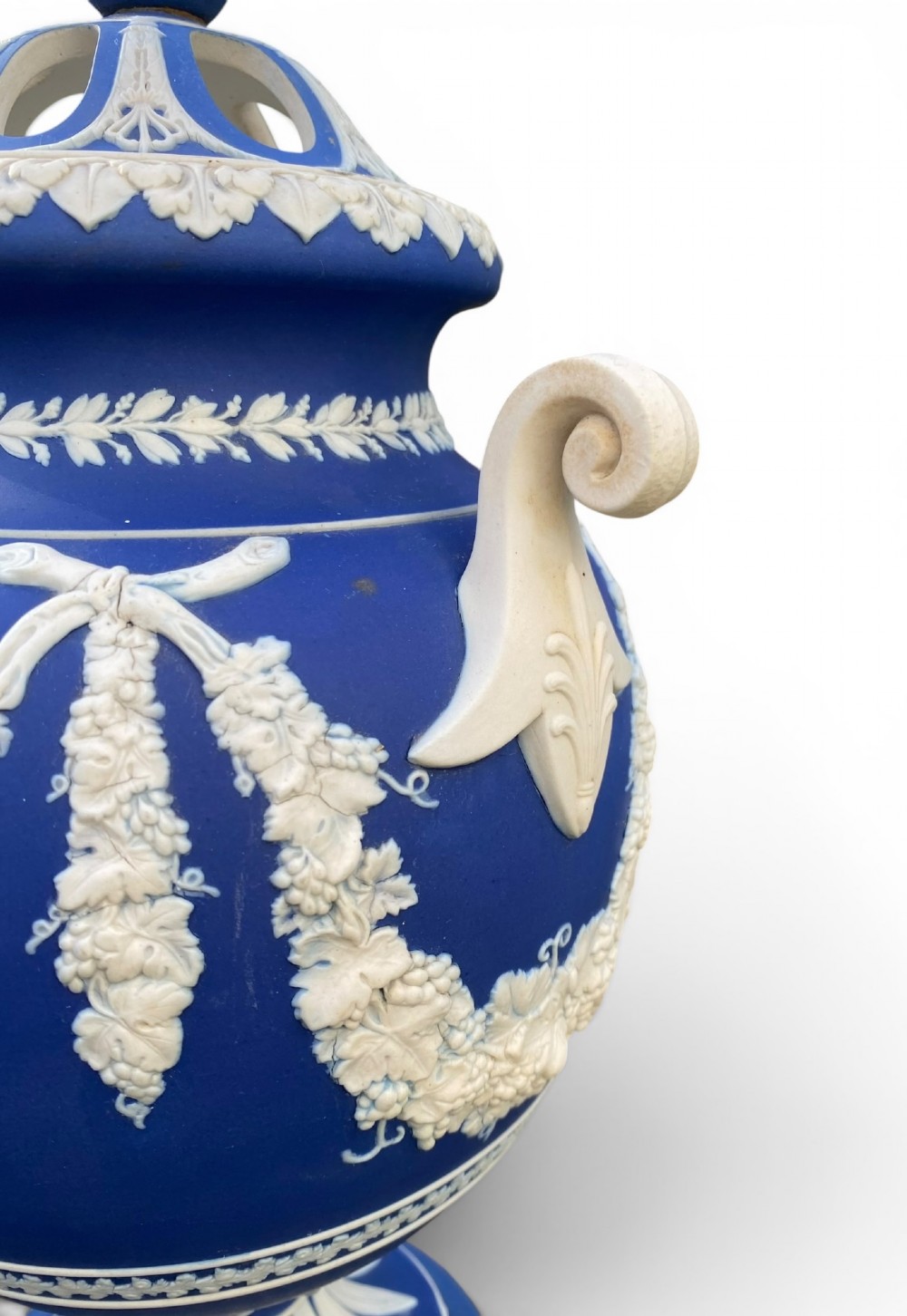 A cobalt blue jasperware pot pourri urn on a matching cylindrical pedestal, featuring white raised relief swags, classical medallions, scroll handles, and a pierced lid. View VI