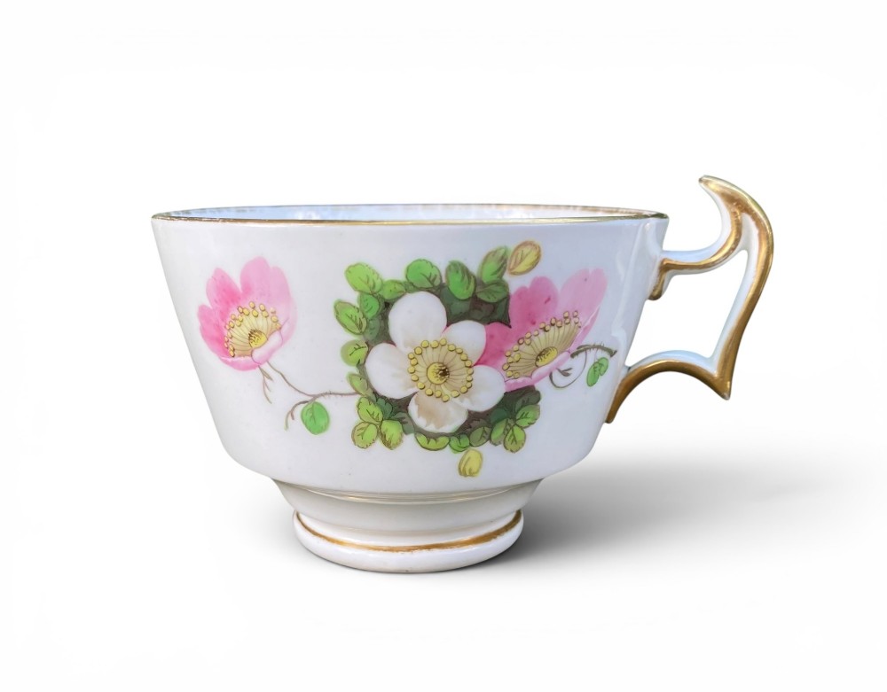 A Regency era white porcelain cup and saucer set decorated with hand-painted pink and white floral motifs and gilded rims. View II