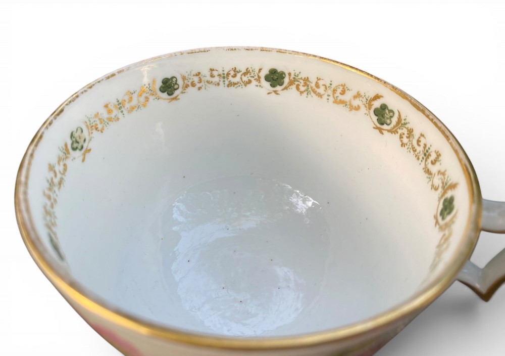 A Regency era white porcelain cup and saucer set decorated with hand-painted pink and white floral motifs and gilded rims. View III