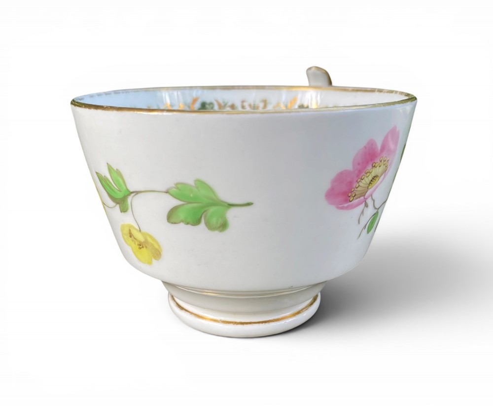 A Regency era white porcelain cup and saucer set decorated with hand-painted pink and white floral motifs and gilded rims. View IV