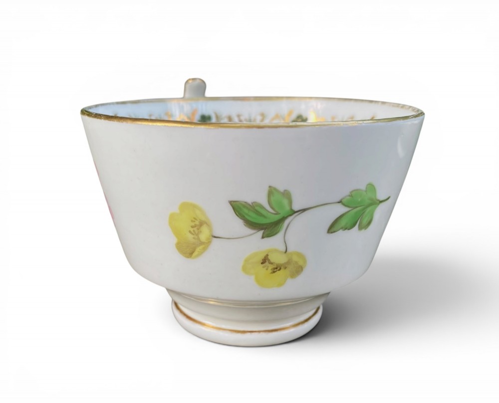 A Regency era white porcelain cup and saucer set decorated with hand-painted pink and white floral motifs and gilded rims. View V