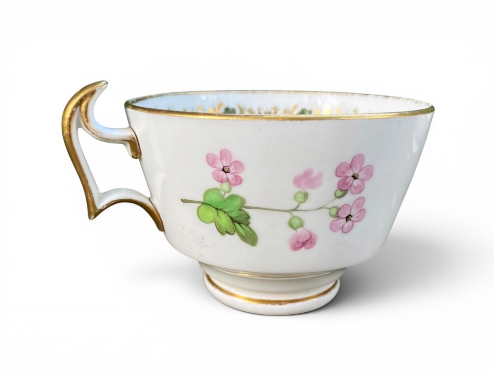 A Regency era white porcelain cup and saucer set decorated with hand-painted pink and white floral motifs and gilded rims. View VI