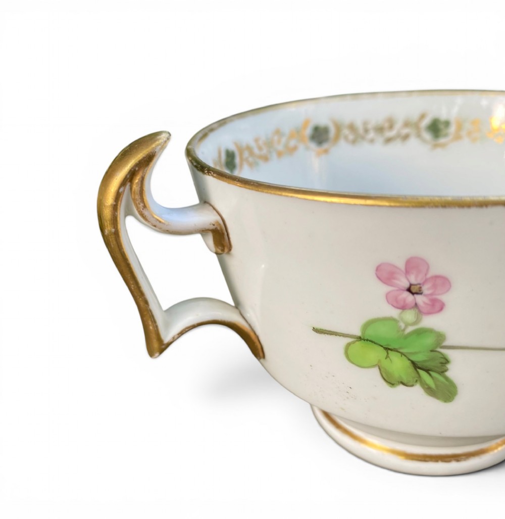 A Regency era white porcelain cup and saucer set decorated with hand-painted pink and white floral motifs and gilded rims. View VII