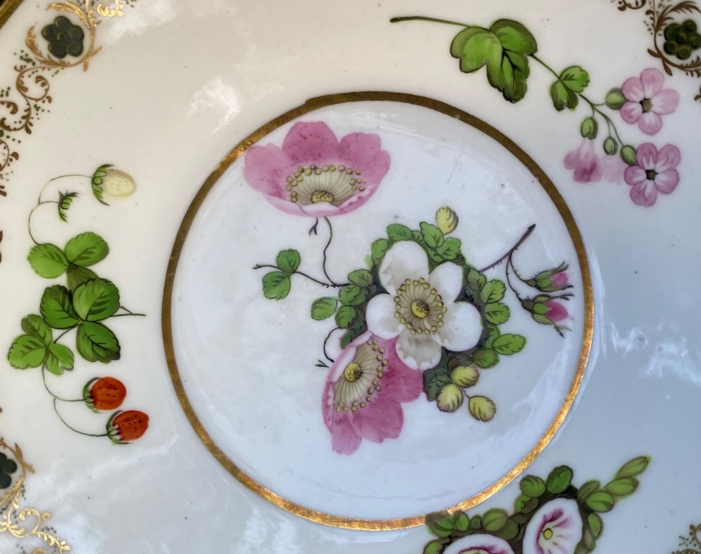 A Regency era white porcelain cup and saucer set decorated with hand-painted pink and white floral motifs and gilded rims. View X