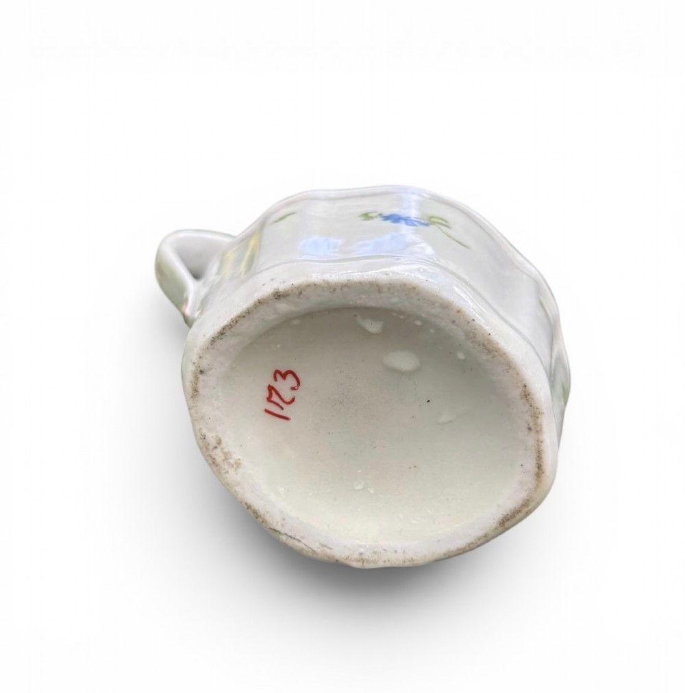 An 18th-century New Hall porcelain cream jug featuring hand-painted floral sprigs, a pink lattice border along the rim, and a faceted lower body with a high loop handle. View II