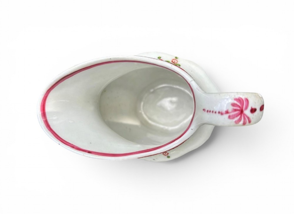 An 18th-century New Hall porcelain cream jug featuring hand-painted floral sprigs, a pink lattice border along the rim, and a faceted lower body with a high loop handle. View III