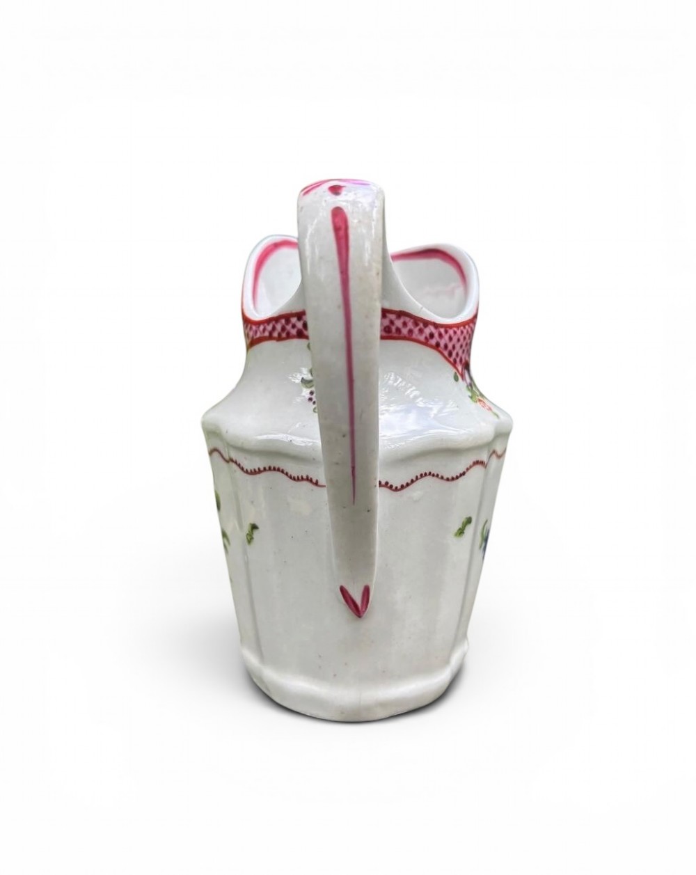 An 18th-century New Hall porcelain cream jug featuring hand-painted floral sprigs, a pink lattice border along the rim, and a faceted lower body with a high loop handle. View IV