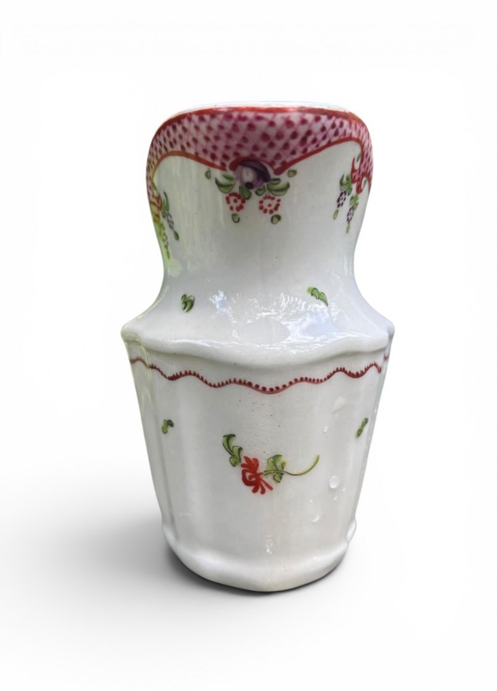 An 18th-century New Hall porcelain cream jug featuring hand-painted floral sprigs, a pink lattice border along the rim, and a faceted lower body with a high loop handle. View VI