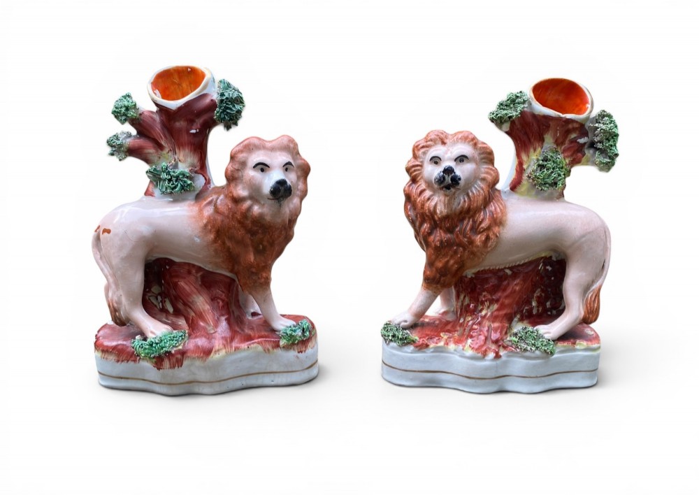 A pair of antique Victorian Staffordshire ceramic spill vases in the form of standing lions beside hollow tree trunks.