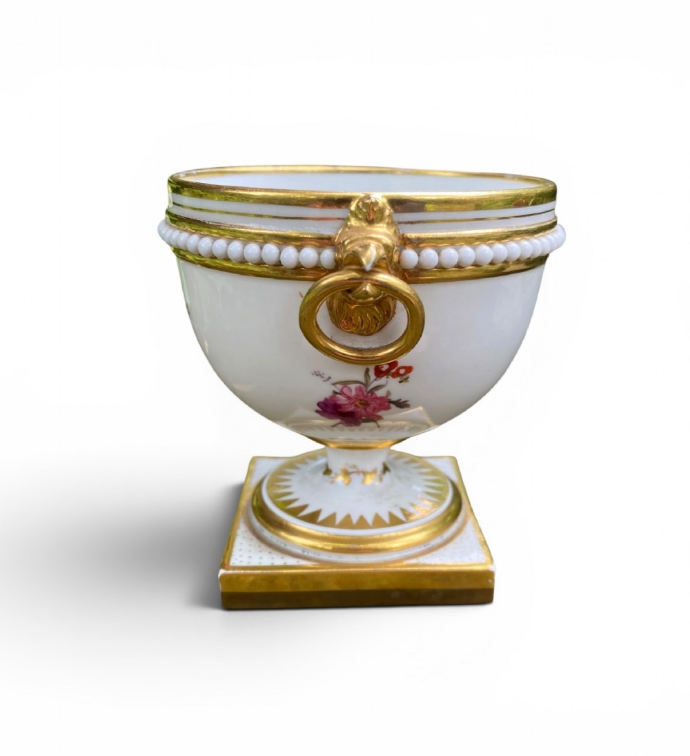 A Regency period white porcelain urn featuring hand-painted botanical blooms, twin gilt handles, a row of pearl-like beaded trimming around the rim, and a gilded square plinth base. View IV