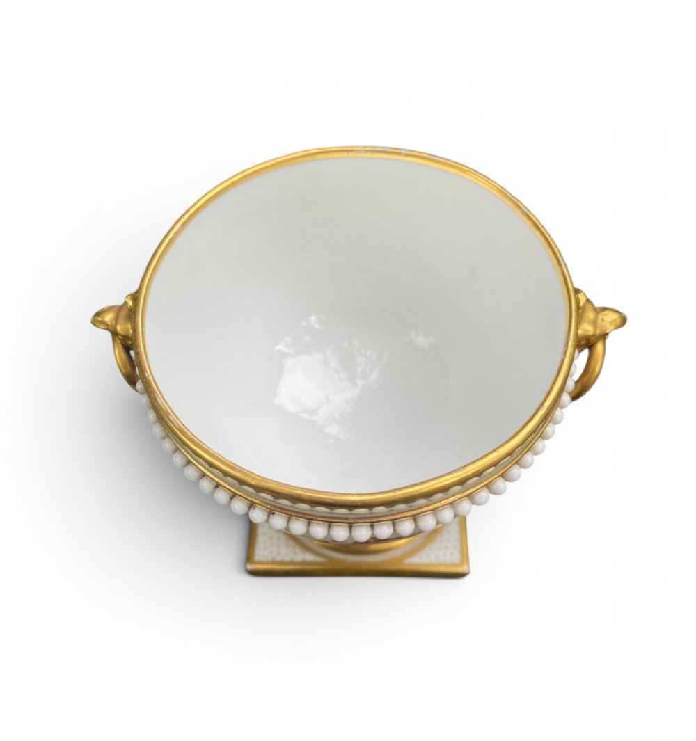 A Regency period white porcelain urn featuring hand-painted botanical blooms, twin gilt handles, a row of pearl-like beaded trimming around the rim, and a gilded square plinth base. View V