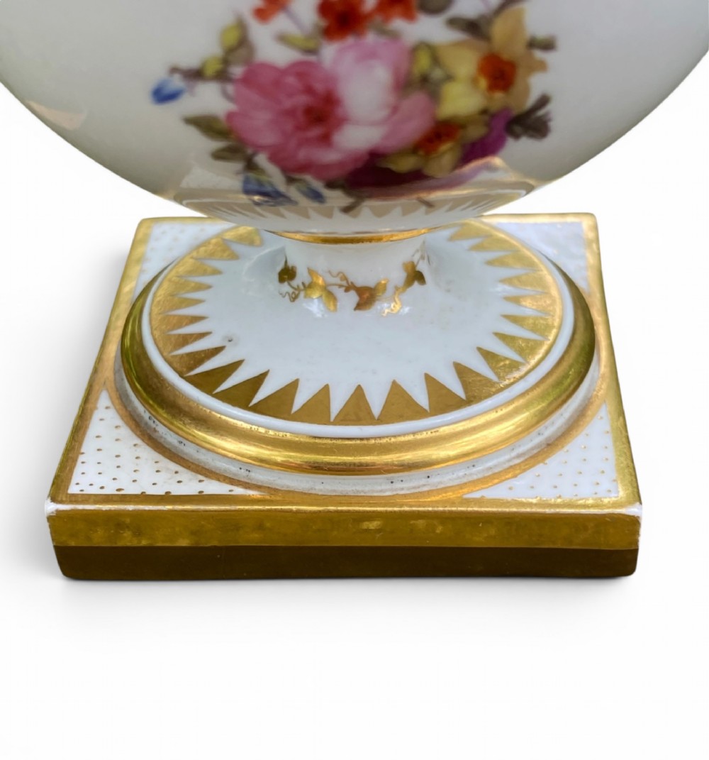 A Regency period white porcelain urn featuring hand-painted botanical blooms, twin gilt handles, a row of pearl-like beaded trimming around the rim, and a gilded square plinth base. View VIII