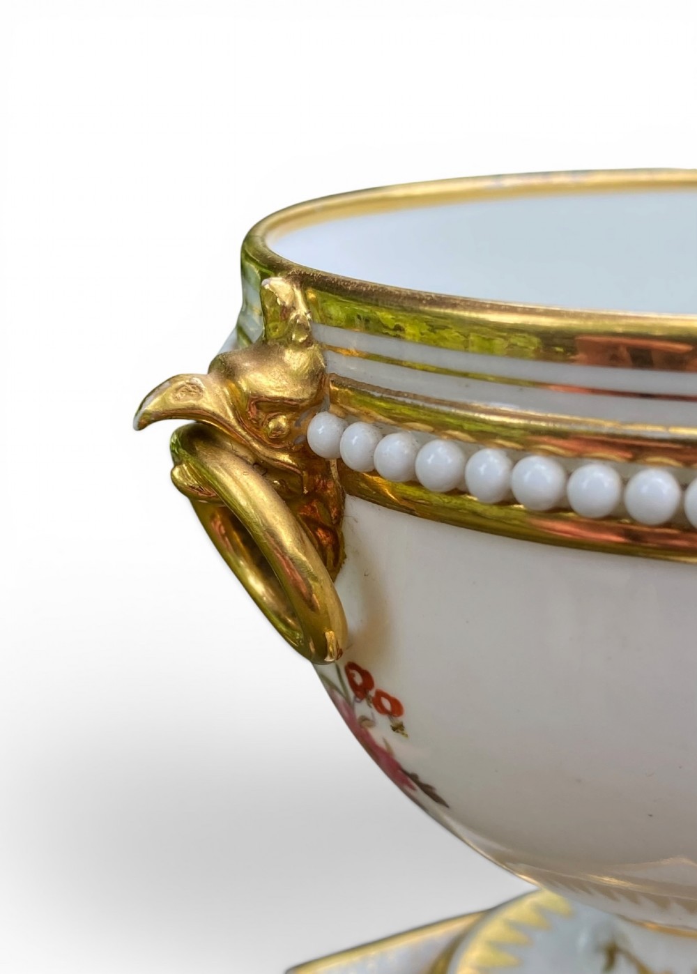 A Regency period white porcelain urn featuring hand-painted botanical blooms, twin gilt handles, a row of pearl-like beaded trimming around the rim, and a gilded square plinth base. View IX