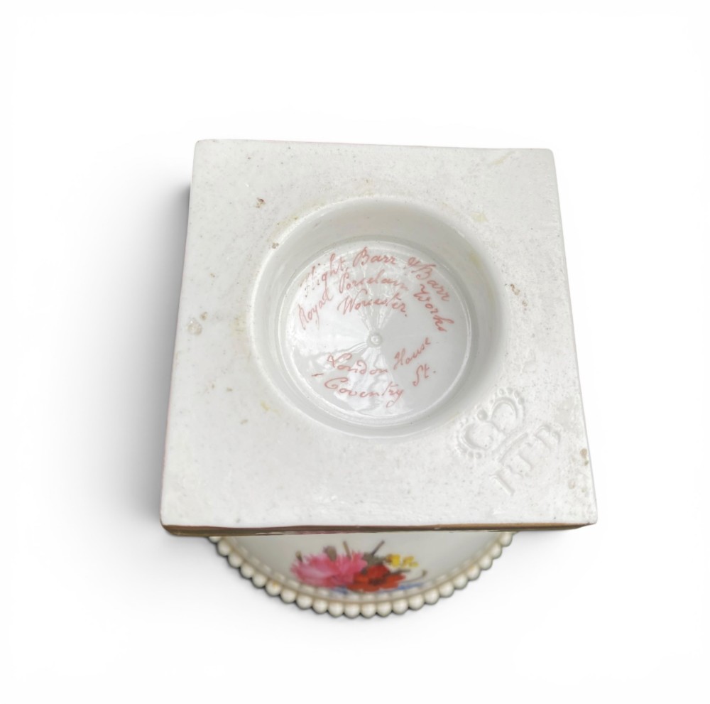 A Regency period white porcelain urn featuring hand-painted botanical blooms, twin gilt handles, a row of pearl-like beaded trimming around the rim, and a gilded square plinth base. View X