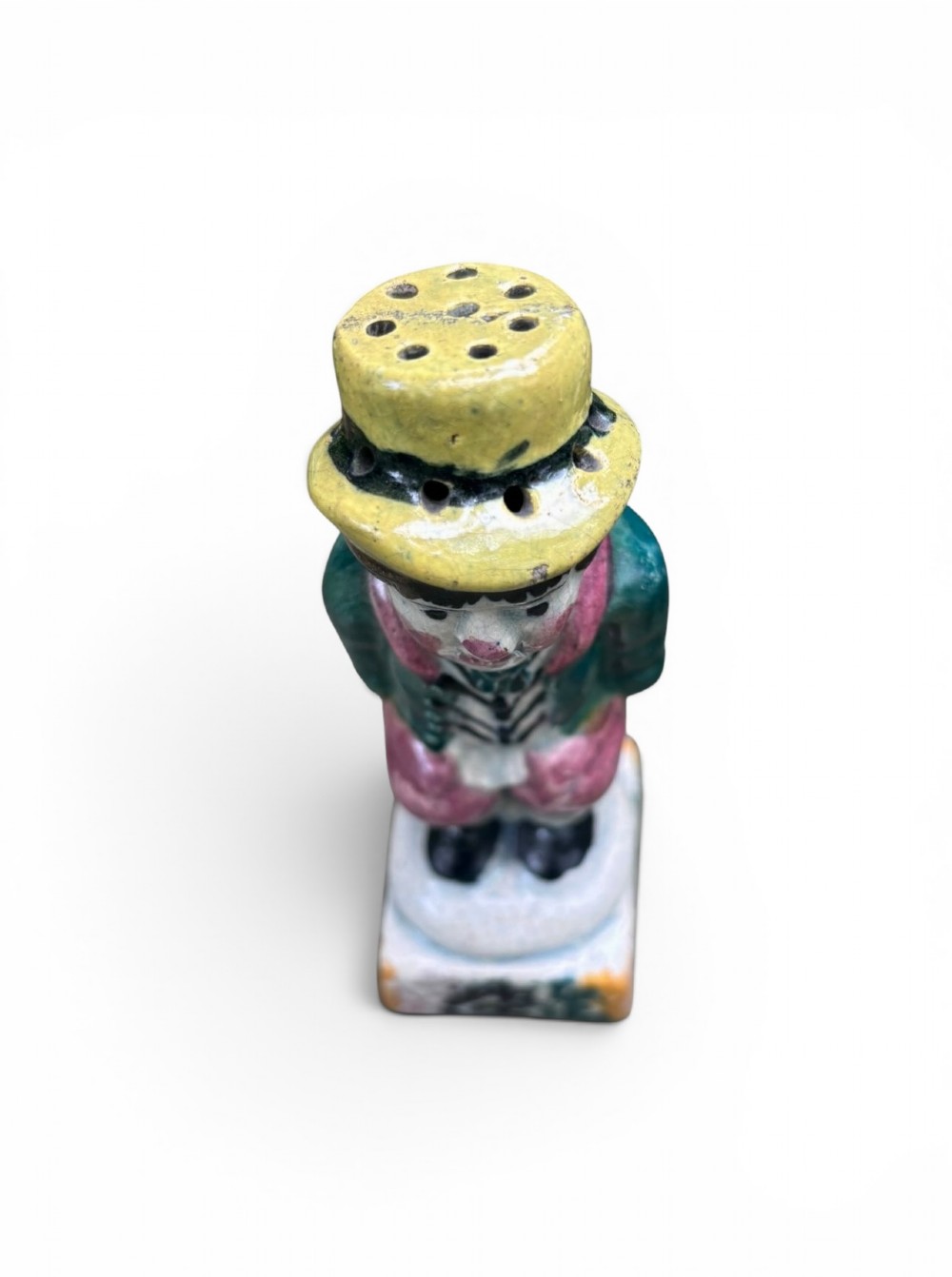 An antique ceramic Prattware figural pepper pot depicting a male character in a yellow top hat, green coat, and pink trousers on a square base. View IV