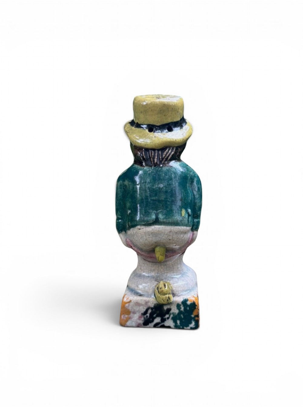 An antique ceramic Prattware figural pepper pot depicting a male character in a yellow top hat, green coat, and pink trousers on a square base. View V
