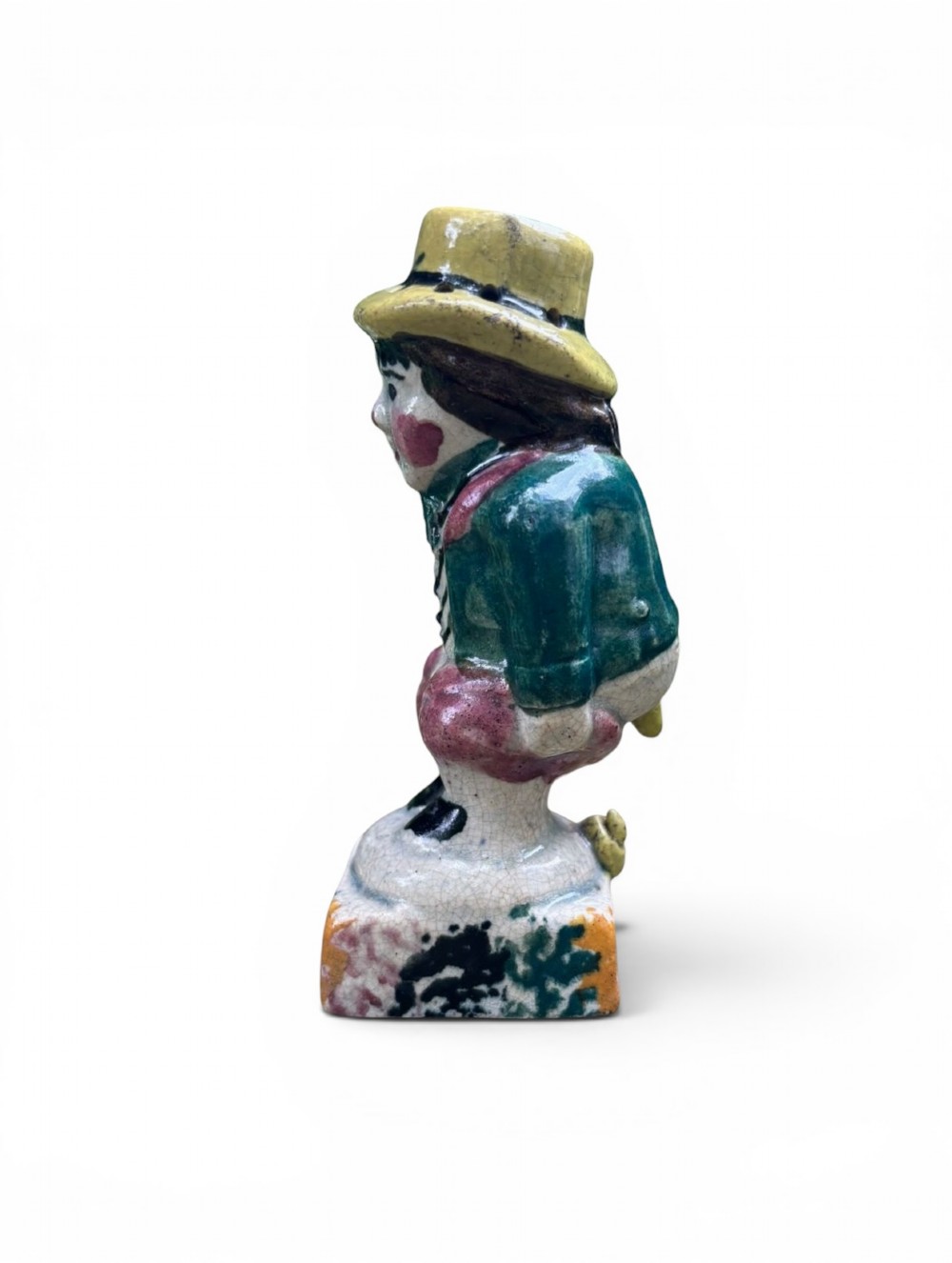 An antique ceramic Prattware figural pepper pot depicting a male character in a yellow top hat, green coat, and pink trousers on a square base. View VI