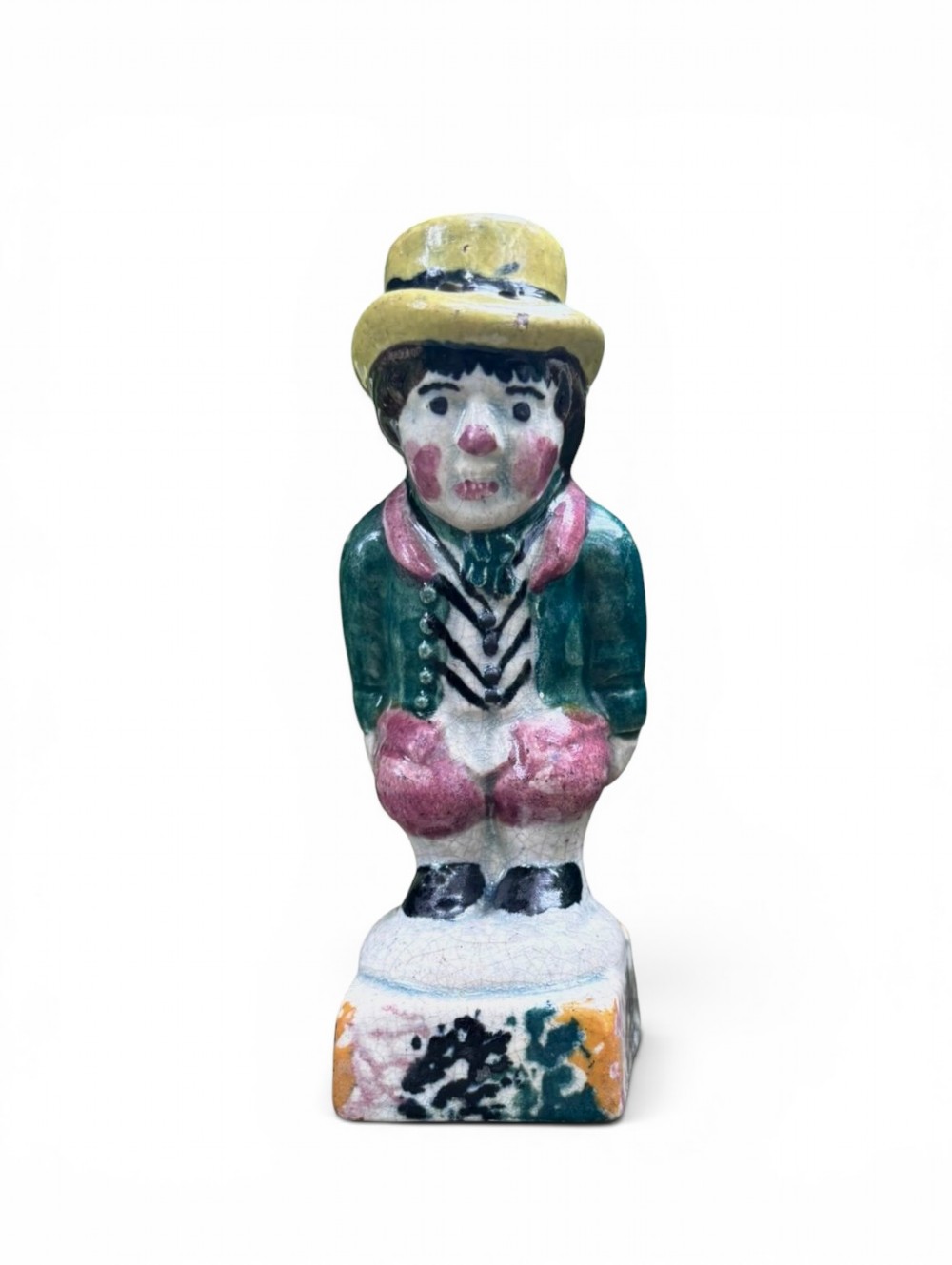 An antique ceramic Prattware figural pepper pot depicting a male character in a yellow top hat, green coat, and pink trousers on a square base. View VII